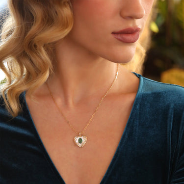Heart-shaped gold pendant with emerald and diamonds, featuring mother of pearl, worn by a woman.