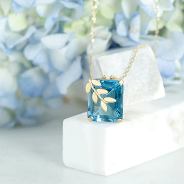 Leaves motif necklace with 11.82ct blue topaz and 0.06ct diamonds in 18K gold, capturing natural elegance.